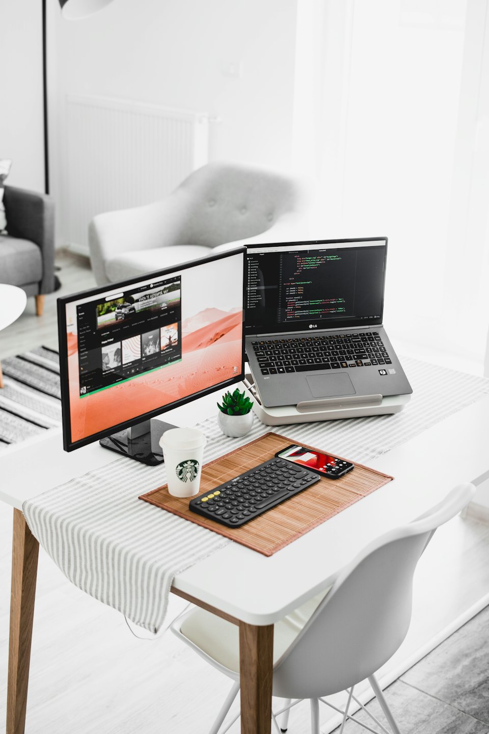 Oficina moderna en casa con portátil, monitor externo mostrando código y accesorios de escritorio.